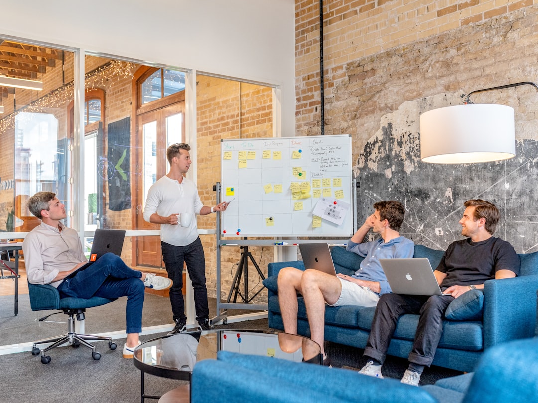 digital three-men-sitting-while-using-laptops-and-watching-man-beside-whiteboard-wd1lrb9oeeo